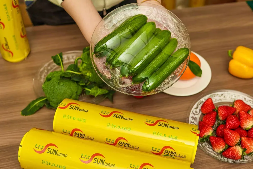 Large-format industrial cling film rolls on a stainless-steel dispenser in a restaurant kitchen and a meat-processing line